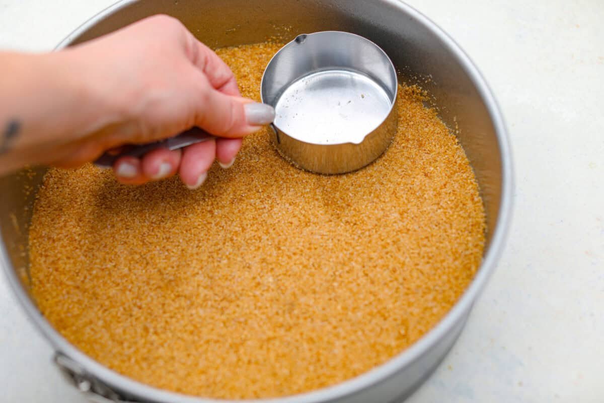 Creme Brulee Cheesecake is the perfect merging of two beloved desserts! It has the rich, creamy texture of cheesecake with the caramelized sugar topping of classic crème brûlée. This irresistible treat is the best of both worlds! Pressing graham cracker crumbs into a springform pan.