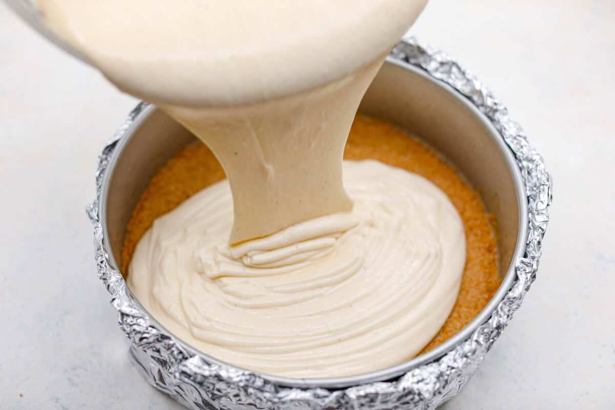 Creme Brulee Cheesecake is the perfect merging of two beloved desserts! It has the rich, creamy texture of cheesecake with the caramelized sugar topping of classic crème brûlée. This irresistible treat is the best of both worlds! Pouring cheesecake mixture into a pan.