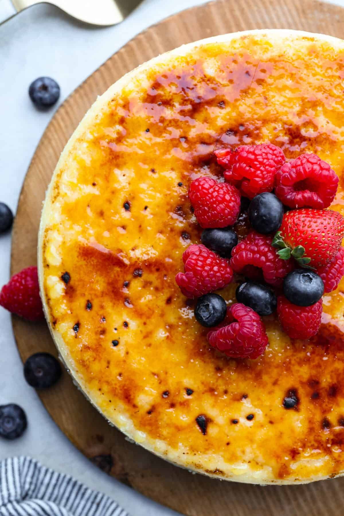 Creme Brulee Cheesecake is the perfect merging of two beloved desserts! It has the rich, creamy texture of cheesecake with the caramelized sugar topping of classic crème brûlée. This irresistible treat is the best of both worlds! Overhead shot of creme brûlée cheesecake with berries on top.