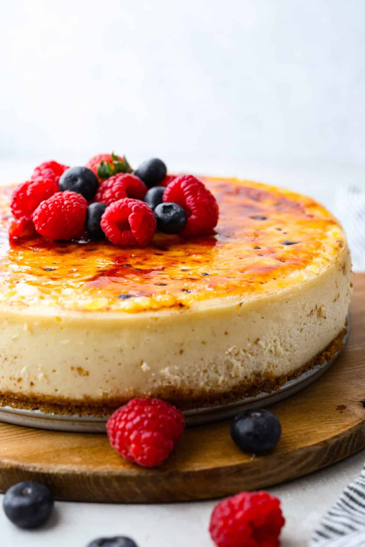Creme Brulee Cheesecake is the perfect merging of two beloved desserts! It has the rich, creamy texture of cheesecake with the caramelized sugar topping of classic crème brûlée. This irresistible treat is the best of both worlds! Creme brûlée cheesecake with fresh raspberries and blueberries on top.