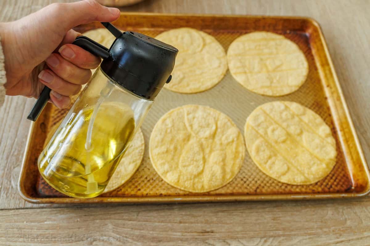 My Baked Chicken Tacos recipe is a fast and delicious 30-minute meal using rotisserie chicken and Rotel for an out-of-this world easy dinner! Tortillas on a baking sheet with olive oil spray to make them crispy