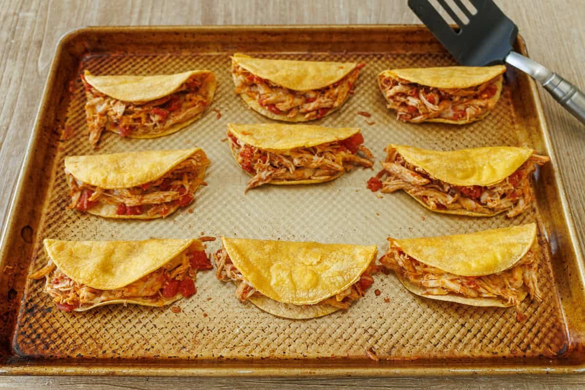 My Baked Chicken Tacos recipe is a fast and delicious 30-minute meal using rotisserie chicken and Rotel for an out-of-this world easy dinner! Folded and Baked Chicken tacos on a sheet pan with spatula for folding
