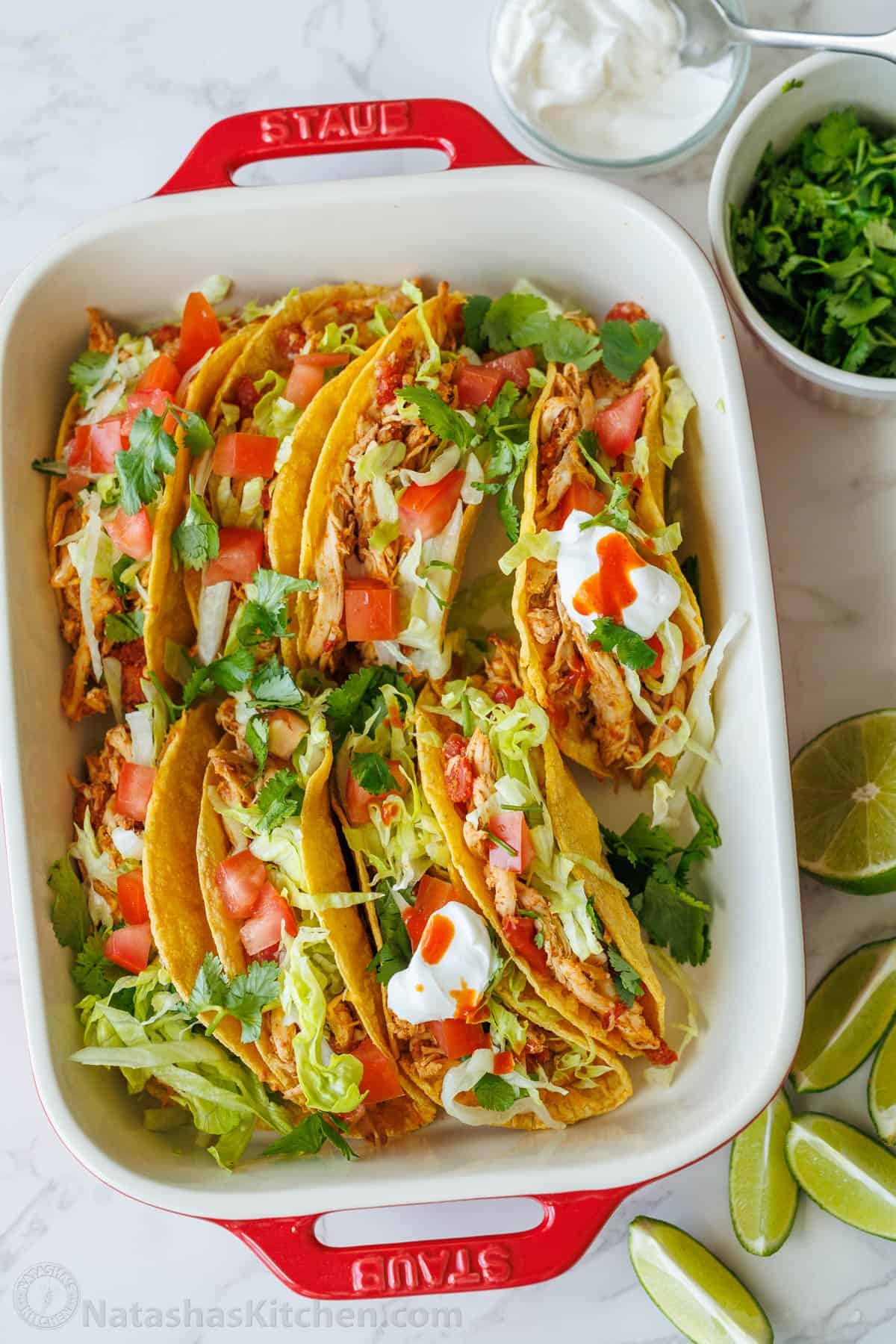 Baked Chicken Tacos are a fast and delicious 30-min meal with shredded chicken over cheesy, crisp tortillas - just add your favorite toppings! Casserole dish Baked Chicken Tacos lined up inside with toppings