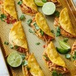 baked chicken tacos on a baking sheet garnished with cilantro and lime