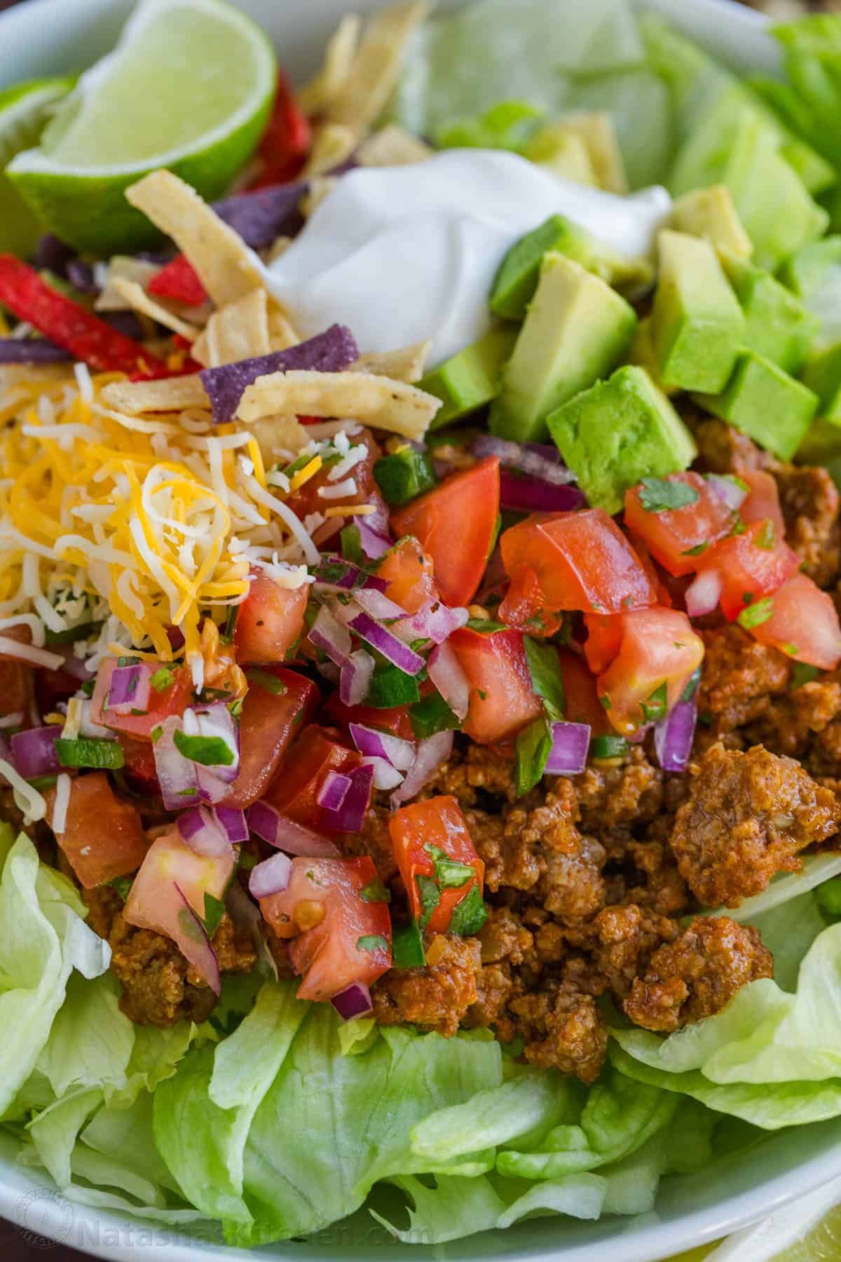 Fresh and easy Taco Salad is loaded with beef, crisp lettuce, veggies, and toppings. Easy 30-minute Taco Salad - perfect for Taco Tuesdays! Taco Salad toppings up close over a bed of iceberg lettuce