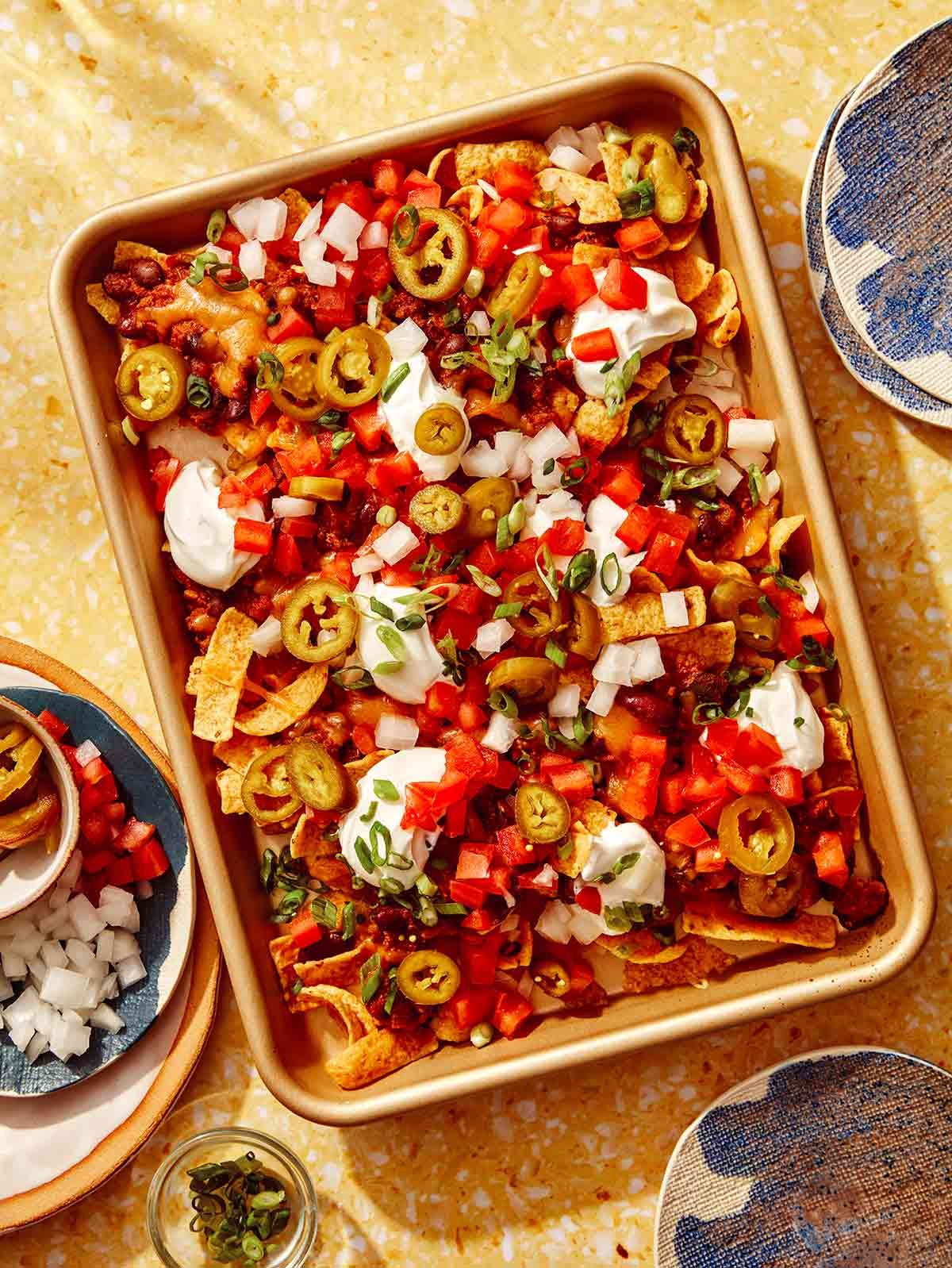 Frito pie on a baking sheet with plates of frito pie around it.