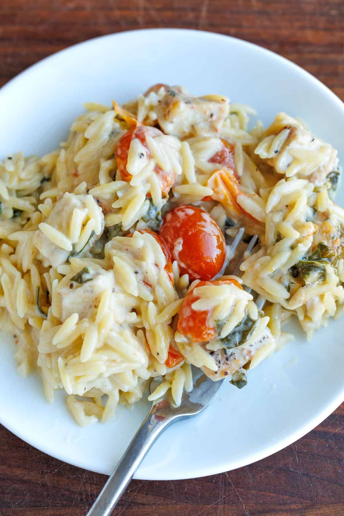This Chicken Orzo Bake is an easy casserole that's creamy and cheesy. Mix it right in the dish, top it with cheese, and bake! Easy meal prep! Chicken pasta casserole on a white dish with a metal spoon