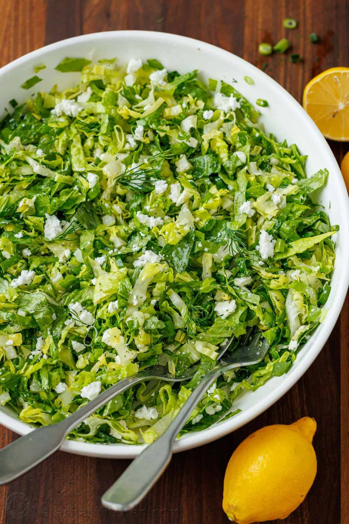 This traditional Maroulosalata recipe is an easy Greek Lettuce Salad with crisp romaine, feta, fresh herbs, and the best lemon dressing! easy Maroulosalata recipe in a white bowl with lemons on a cutting board