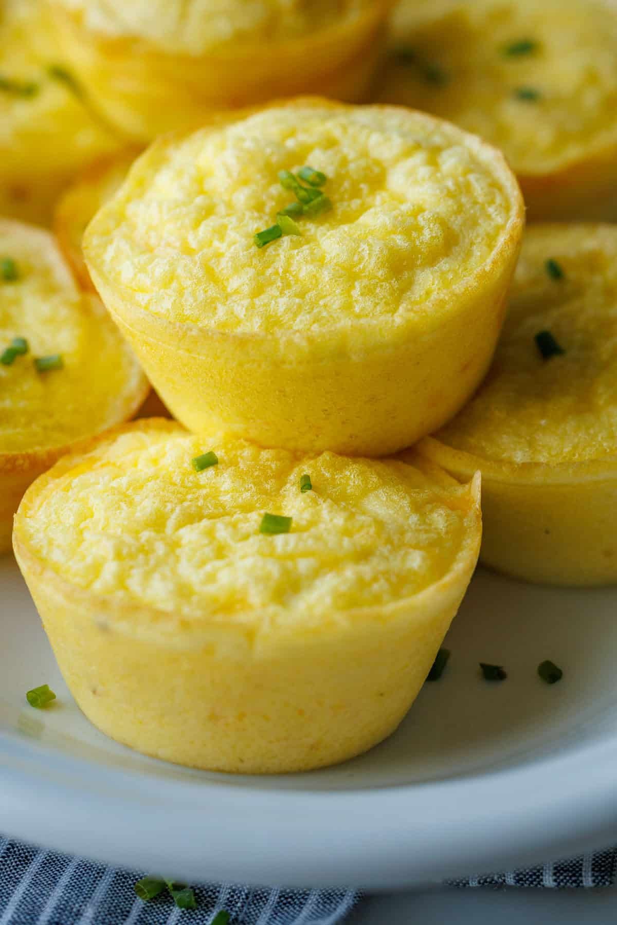 My Cottage cheese egg bites are as good as Starbucks egg bites recipe, but with less hassle! Choose your favorite mix-ins to make them yours. close up of easy breakfast protein muffins stacked on a white plate with chives on top