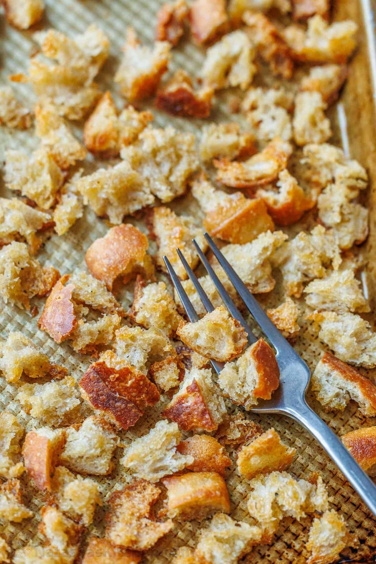 Making Sourdough Croutons is a great way to bring new life to leftover sourdough bread. Use them to bring a delicious crunch to your salads and soups. Sourdough Croutons on a baking sheet with a fork.