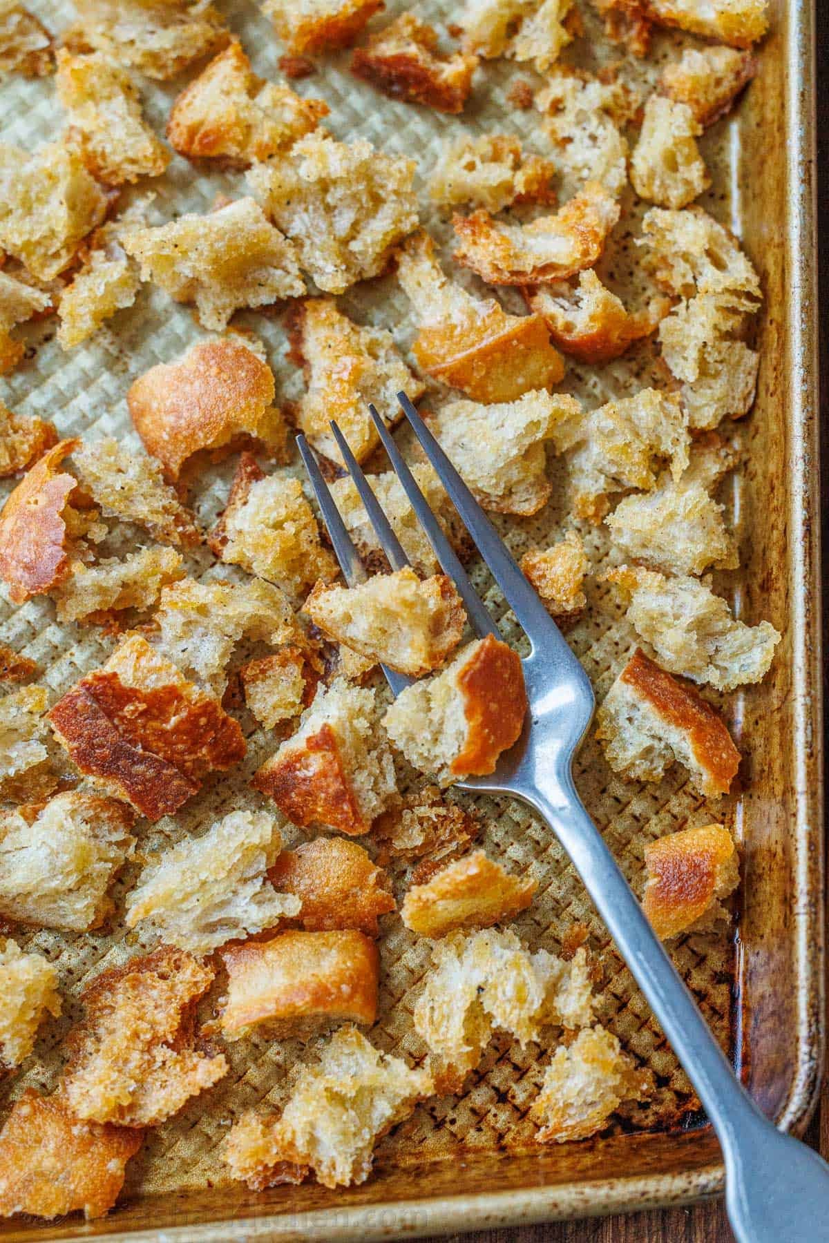 Making Sourdough Croutons is a great way to bring new life to leftover sourdough bread. Use them to bring a delicious crunch to your salads and soups. Sourdough Croutons on a baking sheet with a fork.