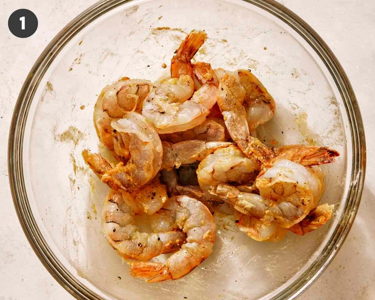 Shrimp seasoned and mixed with oil in a glass bowl.