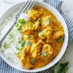Chicken Korma and white rice in a dish with a fork, garnished with chopped cilantro