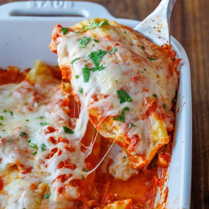 Serving stuffed Manicotti with melted cheese in a white dish