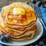 Sourdough Pancakes stacked on a plate with a pad of butter and maple syrup being poured over top.
