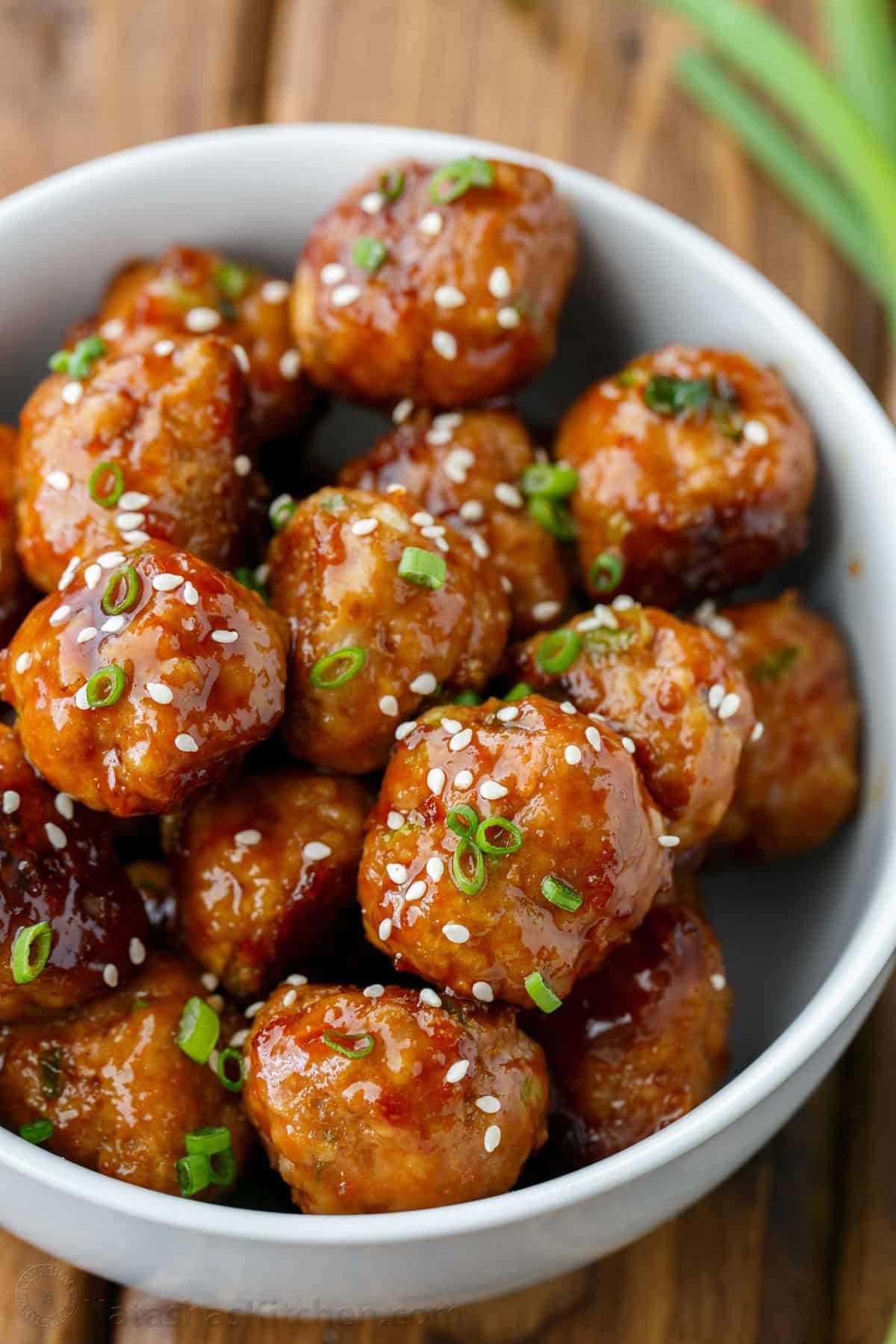 30-minute Turkey Teriyaki Meatballs are just as juicy with less guilt! Simply bake the meatballs and cover them with homemade teriyaki glaze. Teriyaki meatballs in a white bowl garnished with sesame seeds and chives
