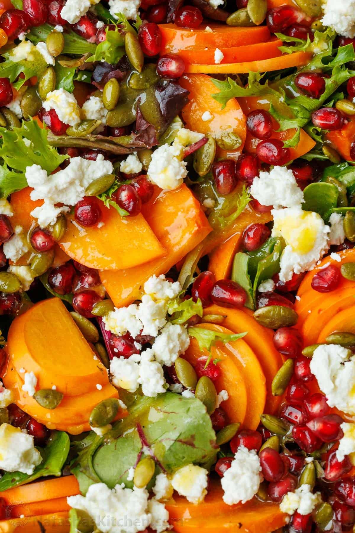 My persimmon Salad recipe features fresh fruit, crunchy toasted pepitas, tangy goat cheese, and a maple vinaigrette. Festive for any holiday! Close up of Persimmon Salad with Maple Vinaigrette with pomegranate seeds, goat cheese and persimmon slices
