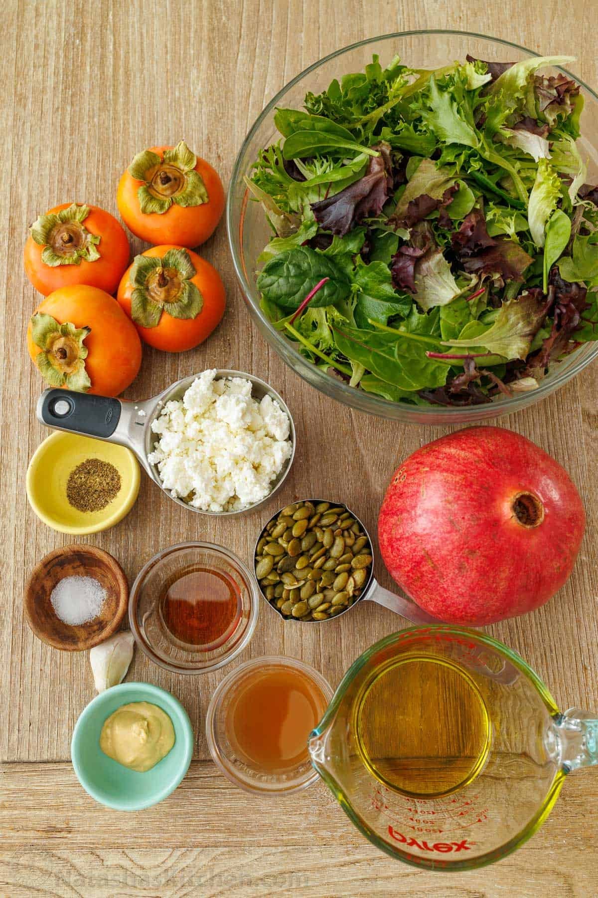 My persimmon Salad recipe features fresh fruit, crunchy toasted pepitas, tangy goat cheese, and a maple vinaigrette. Festive for any holiday! ingredients for the best holiday side dish using mixed greens, winter fruit, pomegranate, goat cheese, salt, pepper, olive oil, maple syrup, dijon mustard, pepitas, and apple cider vinegar