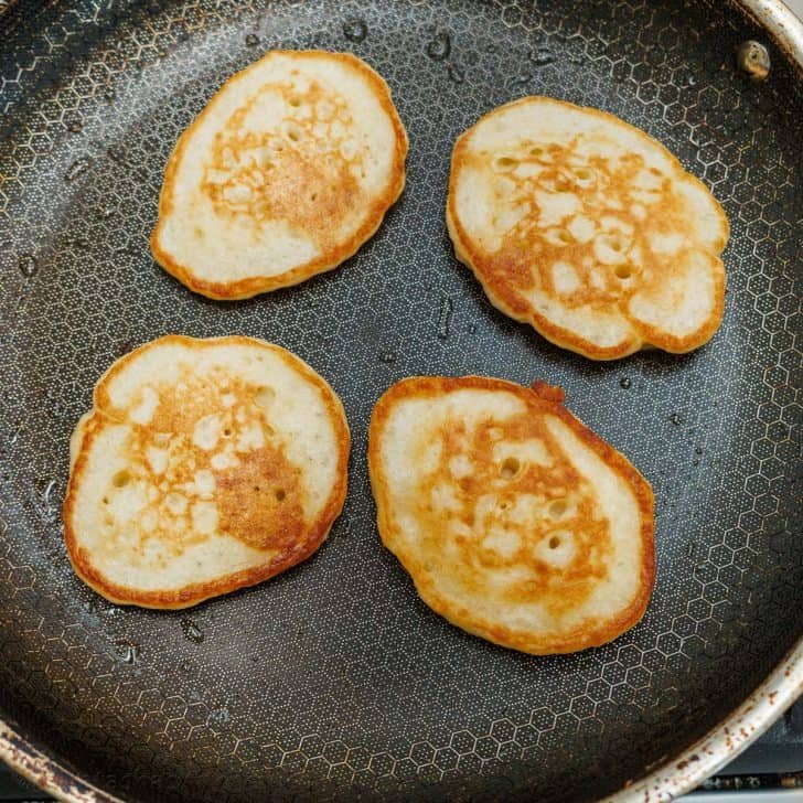 Sourdough Pancakes are a delightful twist on the classic breakfast favorite, with a soft and spongy texture and great sourdough flavor. Four sourdough pancakes on a hot skillet, cooked to golden perfection.