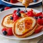Sourdough discard pancakes stacked on a plate with fresh berries and drizzled honey