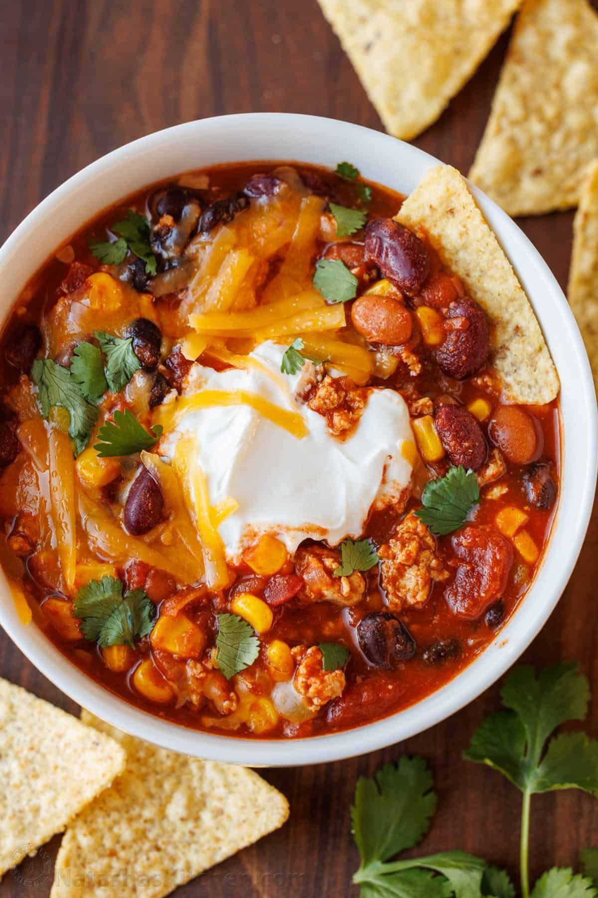 The best Turkey Chili recipe - easy (mostly dump & simmer) and loaded with turkey, beans, and veggies. It's perfect for busy weeknights! Bowl of turkey chili garnished with sour cream and chips