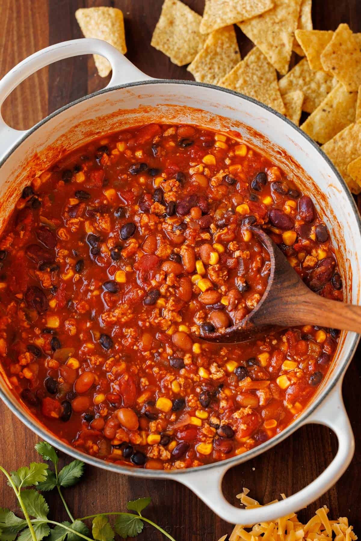 The best Turkey Chili recipe - easy (mostly dump & simmer) and loaded with turkey, beans, and veggies. It's perfect for busy weeknights! pot of turkey chili in a Dutch Oven with chips on the side