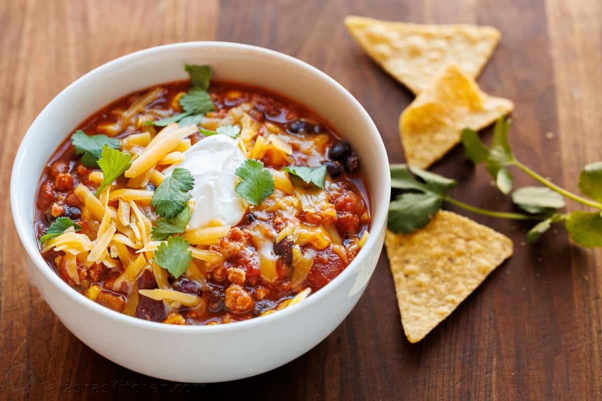 My turkey chili recipe is so easy to make in 40 minutes on the stovetop or slow cooker. Ground turkey, beans and veggies make it a favorite! white bowl of turkey chili with cheese and sour cream on top and corn chips on the side