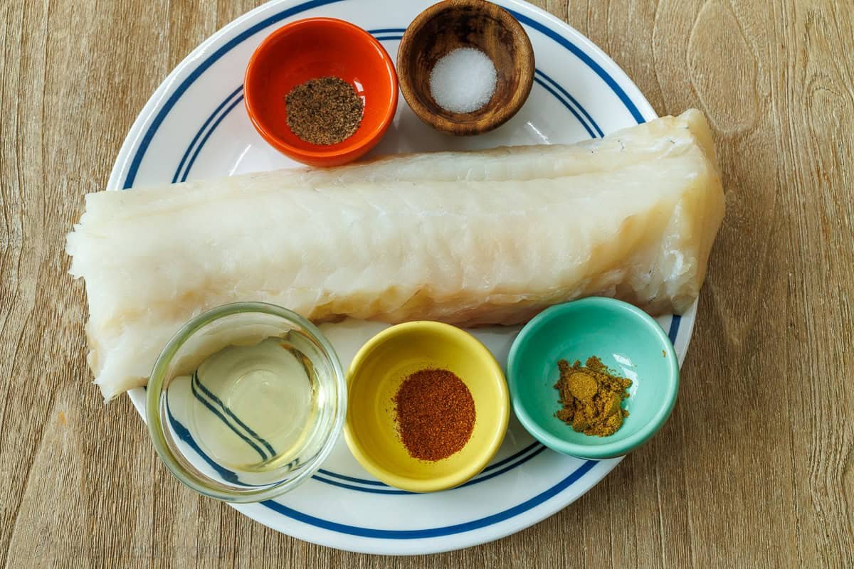 Our Fish Taco Bowl recipe is an easy taco night recipe. Mix flaky fish, Cilantro Lime Rice, toppings, and crema Sauce to serve in 30 minutes. Ingredients for Fish Taco Bowls including filet of white fish, olive oil, and Taco seasonings on a white plate