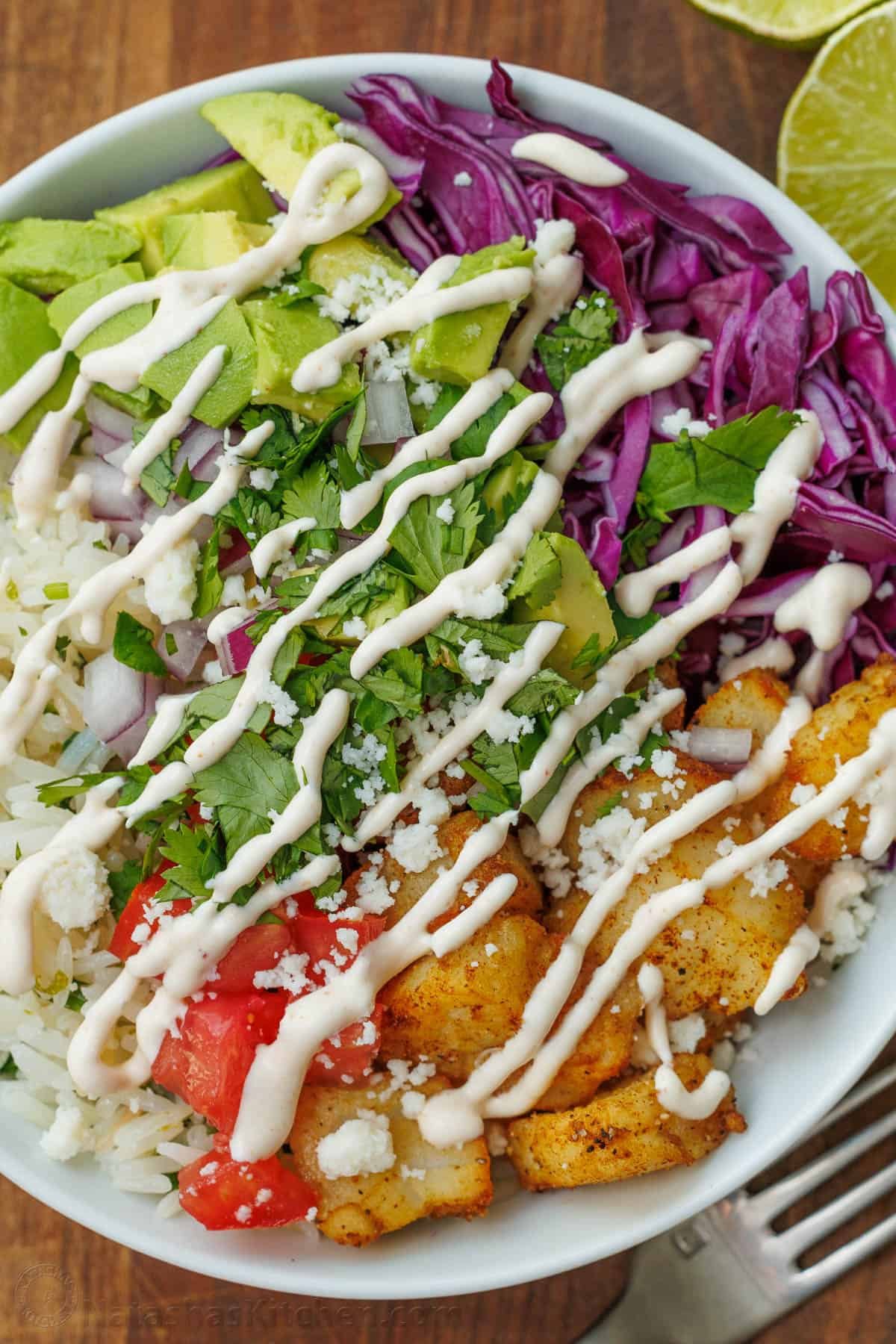 Our Fish Taco Bowl recipe is an easy taco night recipe. Mix flaky fish, Cilantro Lime Rice, toppings, and crema Sauce to serve in 30 minutes. Fish taco bowl with Crema sauce drizzled on top and a fork