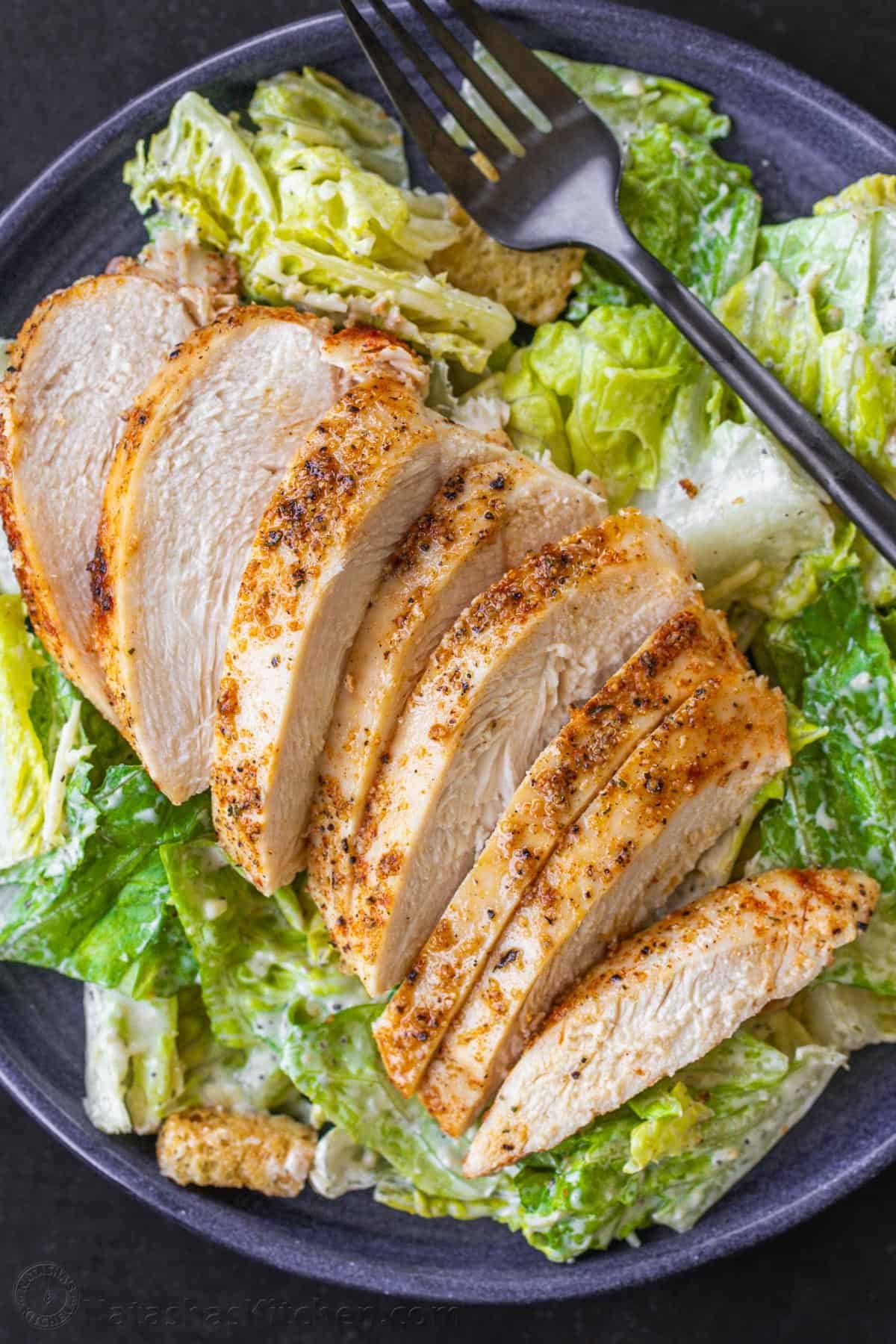 This Baked Chicken Breast is tender, juicy, and perfectly seasoned - versatile and great for meal prep! Say goodbye to dry, boring chicken! Chicken breast on a plate with Caesar salad.