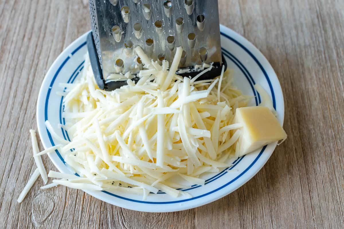 Creamy Au Gratin Potatoes are made with thinly sliced potatoes baked in a rich cheese sauce. Potato Gratin is an impressive holiday side dish. Freshly grated Gruyere cheese on a plate next to a box grater.