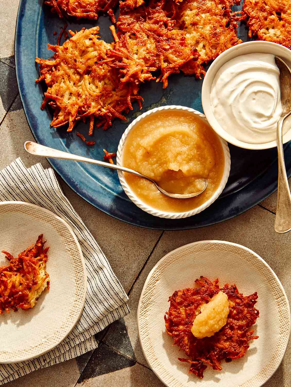 Potato latkes served from a platter with toppings of sour cream and applesauce.