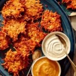 Potato latkes on a platter with sour cream and applesauce on the side.