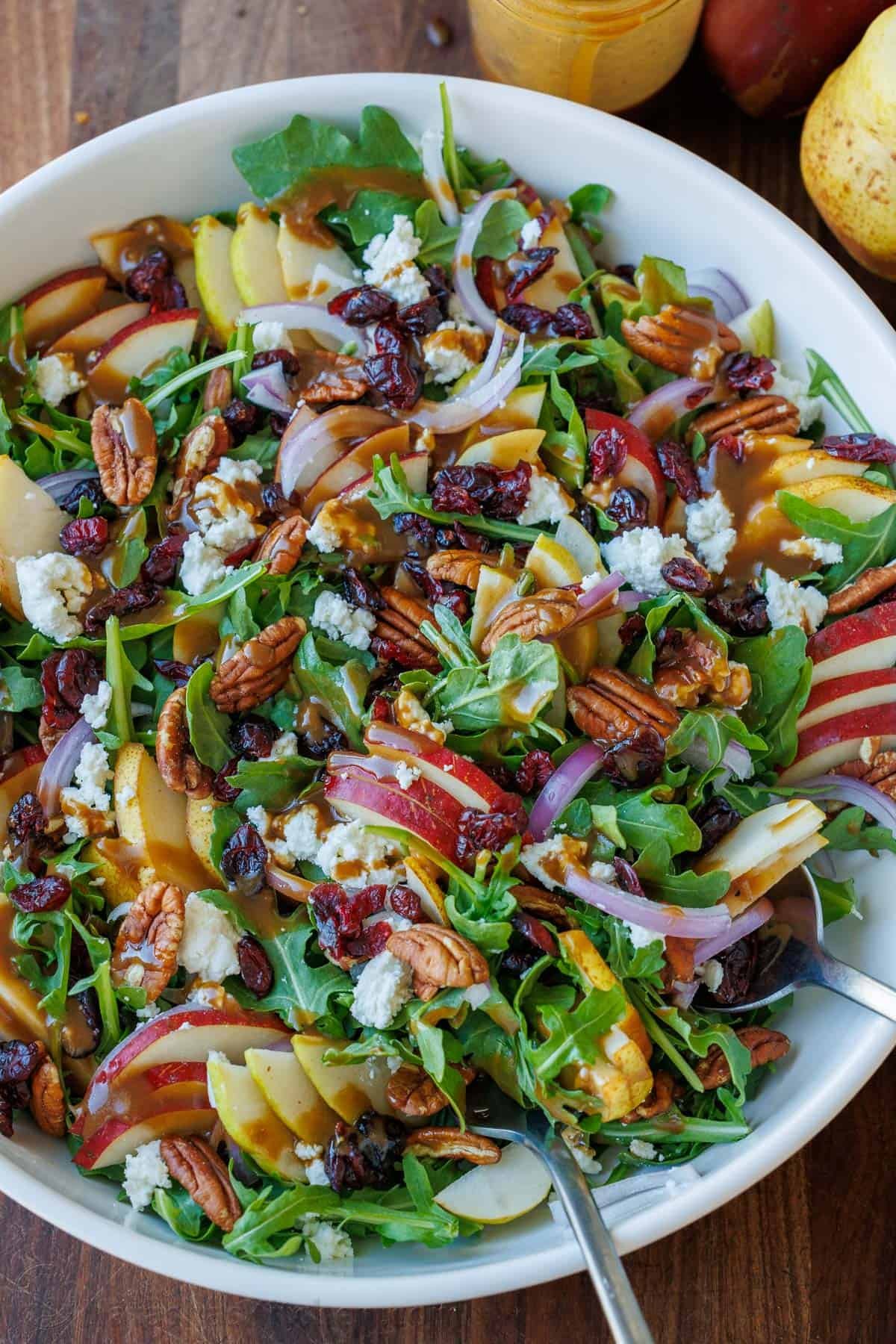 This elegant Pear Salad with Balsamic Vinaigrette is a stunning fall salad featuring sweet pears, peppery arugula, tangy Craisins, toasted pecans, and creamy goat cheese. Autumn Pear Salad with Balsamic Vinaigrette and toasted pecans in a white bowl, loaded with a variety of pears, red onion, goat cheese, and cranberries.