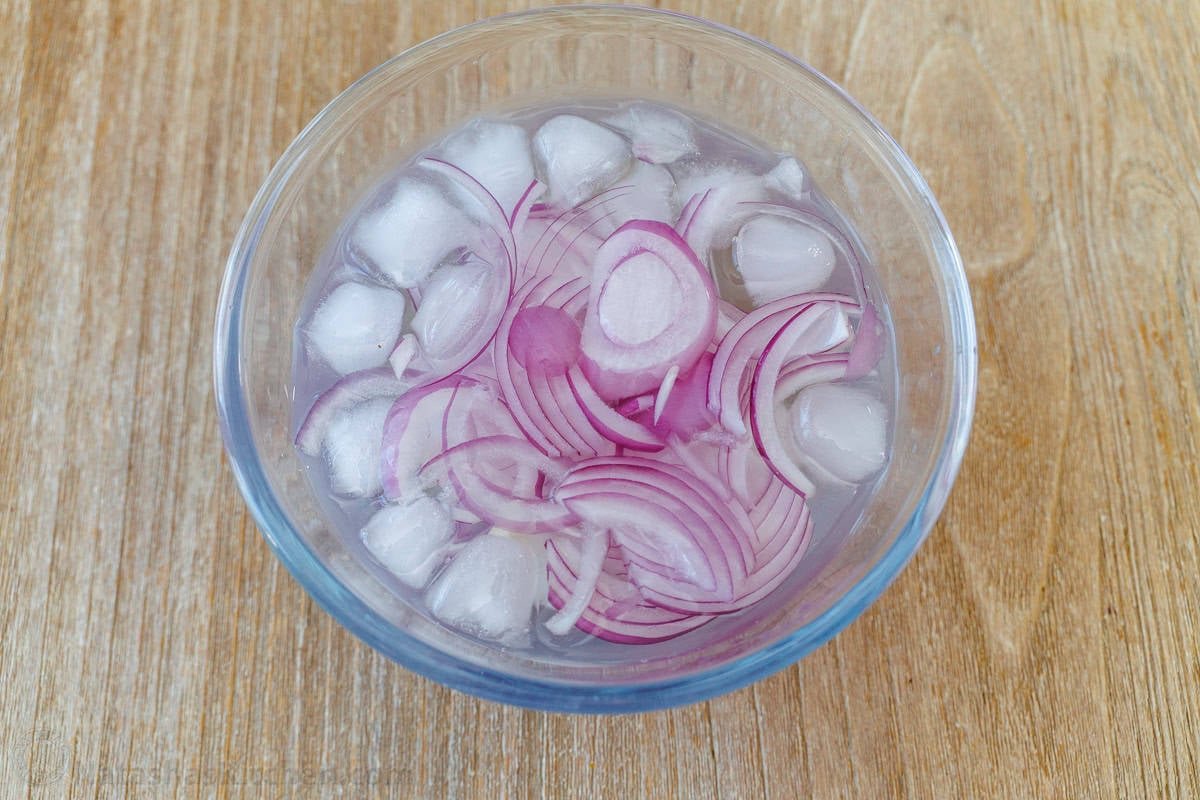 Soaking onions in water with ice helps to remove some of the strong onion flavor Red onions soaking in a glass bowl with water and rice to remove some of its harsh onion flavor