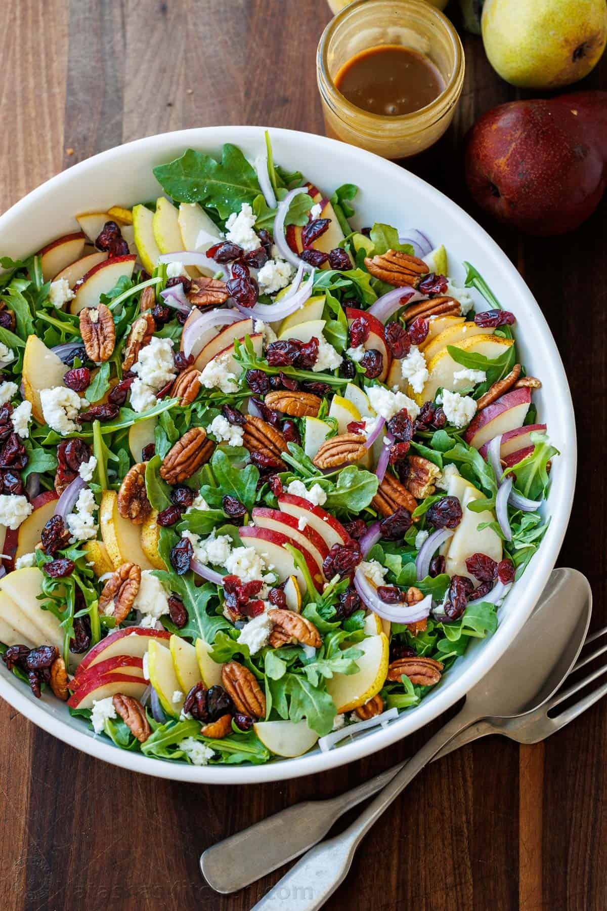 This elegant Pear Salad with Balsamic Vinaigrette is a stunning fall salad featuring sweet pears, peppery arugula, tangy Craisins, toasted pecans, and creamy goat cheese. Pear Salad with Balsamic Vinaigrette in a white bowl, loaded with a variety of pears, red onion, goat cheese, cranberries, and toasted pecans