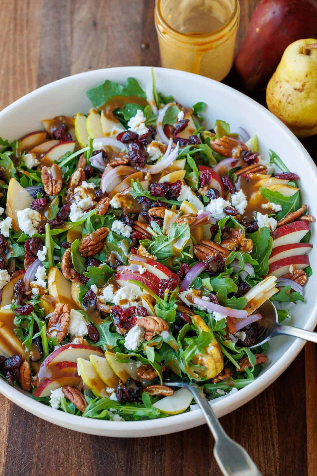 This Autumn Pear Salad is stunning with sweet pears, fresh arugula, tangy Craisins, pecans, goat cheese, and a homemade Balsamic Vinaigrette. Pear Salad drizzled with Balsamic Vinaigrette in a white bowl, loaded with a variety of pears, red onion, goat cheese, cranberries, and toasted pecans
