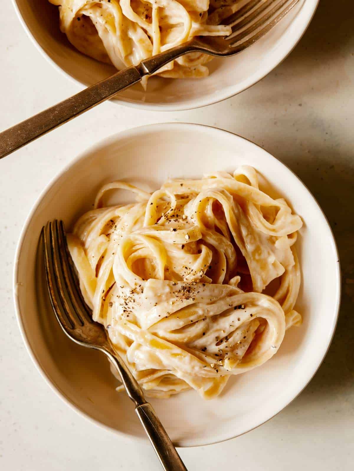Two bowls of fettuccine alfredo with a fork in one.