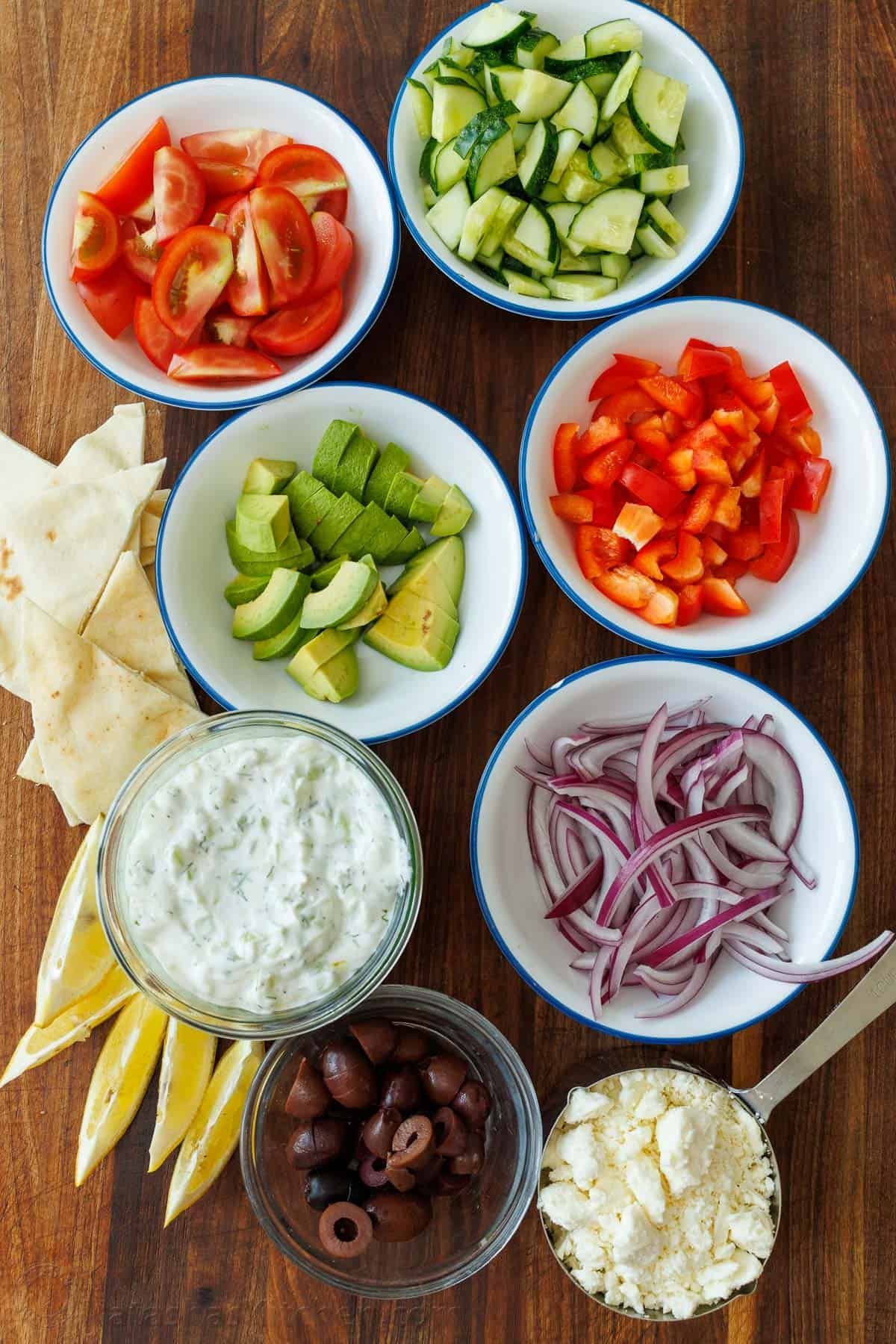 Greek Chicken Bowls combine the classic elements of a Greek Salad—cucumbers, tomatoes, olives, and feta—elevated with juicy grilled chicken and a refreshing dollop of tzatziki. Greek Chicken Bowls salad ingredients: tzatziki sauce, bell pepper, tomatoes, avocado, cucumber, red onion, kalamata olives, feta cheese, lemon wedges