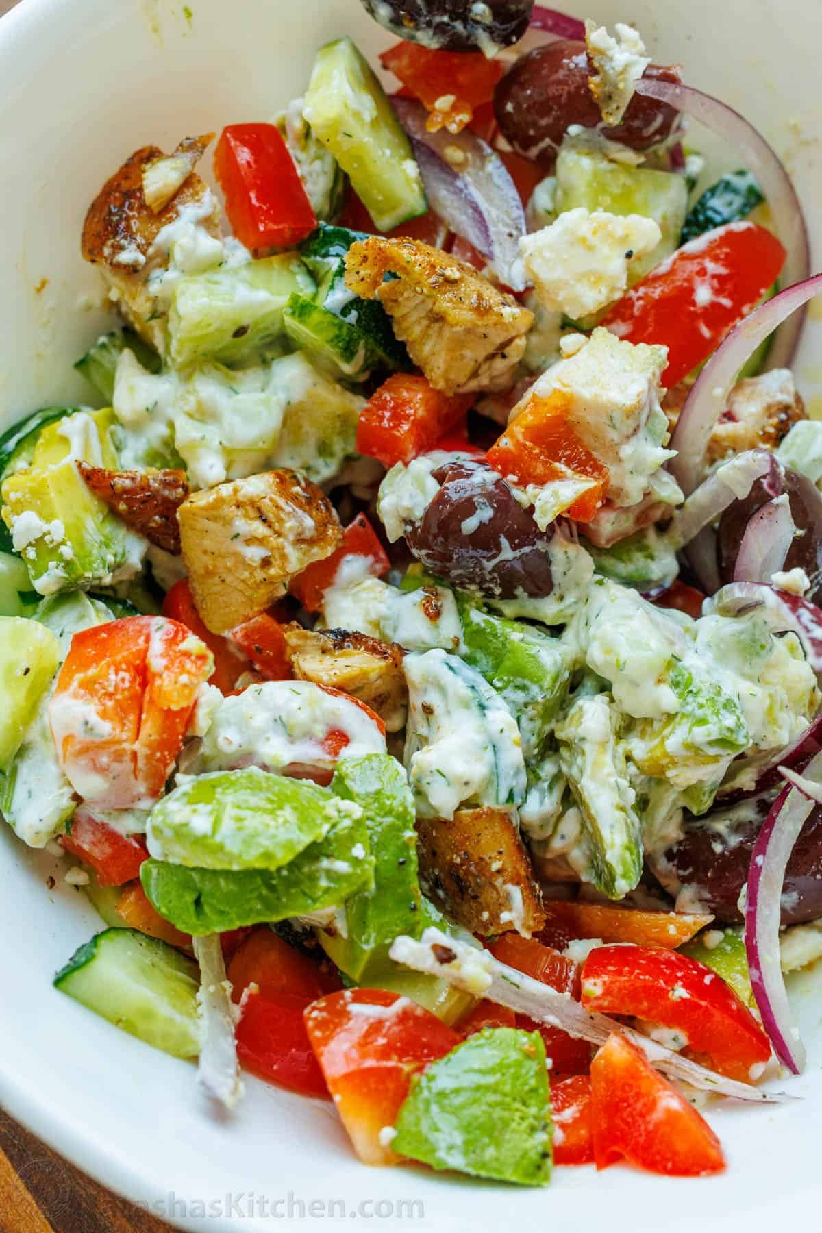 Greek Chicken Bowls combine the classic elements of a Greek Salad—cucumbers, tomatoes, olives, and feta—elevated with juicy grilled chicken and a refreshing dollop of tzatziki. Chopped Greek Chicken Bowl ingredients gently tossed in tzatziki sauce and freshly squeezed lemon juice in a white bowl
