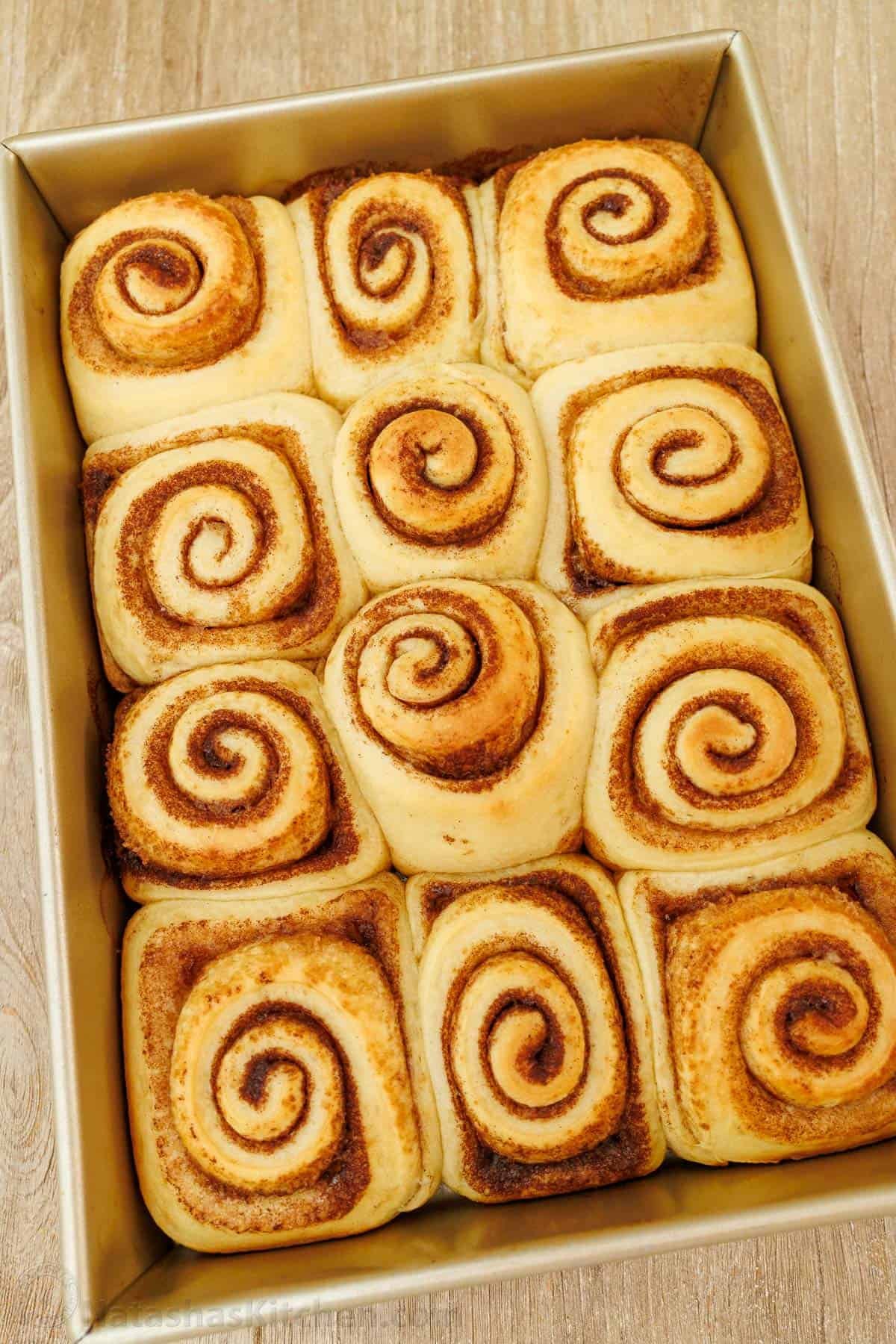 The perfect recipe for soft, fluffy, and buttery Sourdough Cinnamon Rolls, layered with cinnamon sugar and topped with creamy cream cheese frosting. Sourdough Cinnamon rolls freshly baked in a metal baking pan, but not yet frosted. Showing the beautiful cinnamon sugar swirl of each roll.