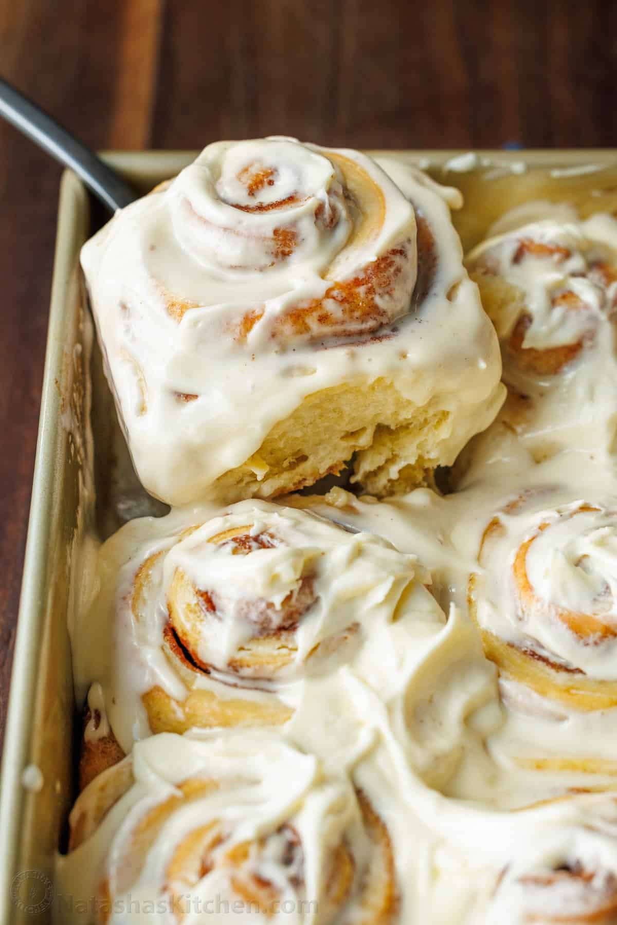 The perfect recipe for soft, fluffy, and buttery Sourdough Cinnamon Rolls, layered with cinnamon sugar and topped with creamy cream cheese frosting. A pan of baked and frosted Sourdough Cinnamon Rolls with one roll being lifted out for serving.