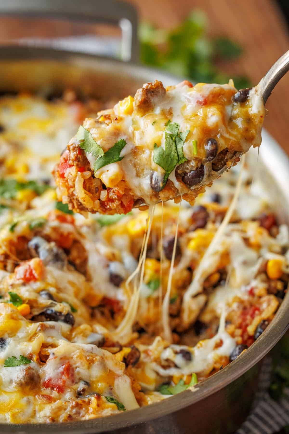 Mexican Beef and Rice Skillet is a quick, 30-minute meal—seasoned beef, loaded rice, and gooey melted cheese. The perfect one-pan wonder! A serving spoon loaded with Mexican Ground Beef and Rice Skillet, showcasing the Mexican cheese pulls.