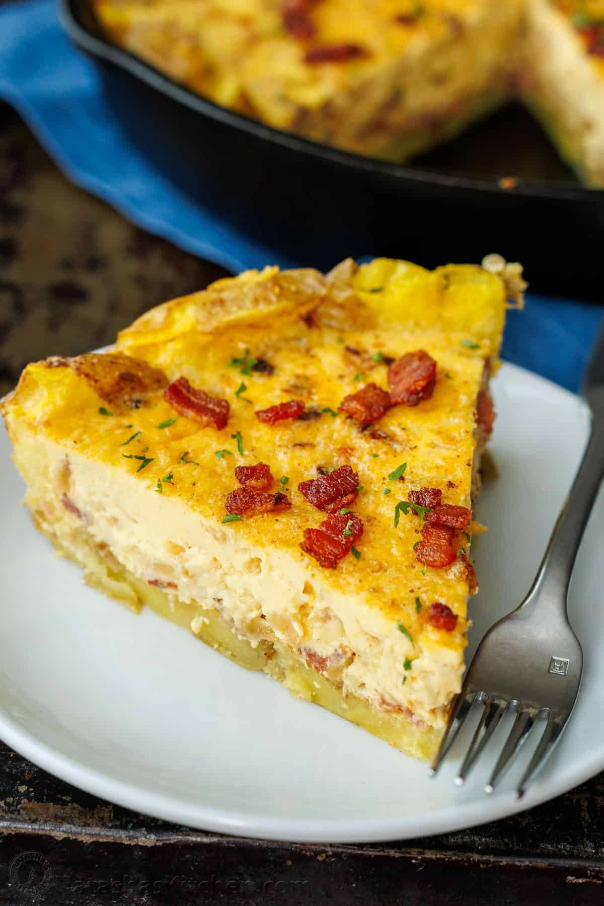 Our Potato Crusted Quiche replaces traditional dough with smashed potatoes for a tasty, gluten-free option that's easy to make and perfect for brunch. A slice of Potato Crusted Quiche topped with bacon and parsley on a plate with a fork.