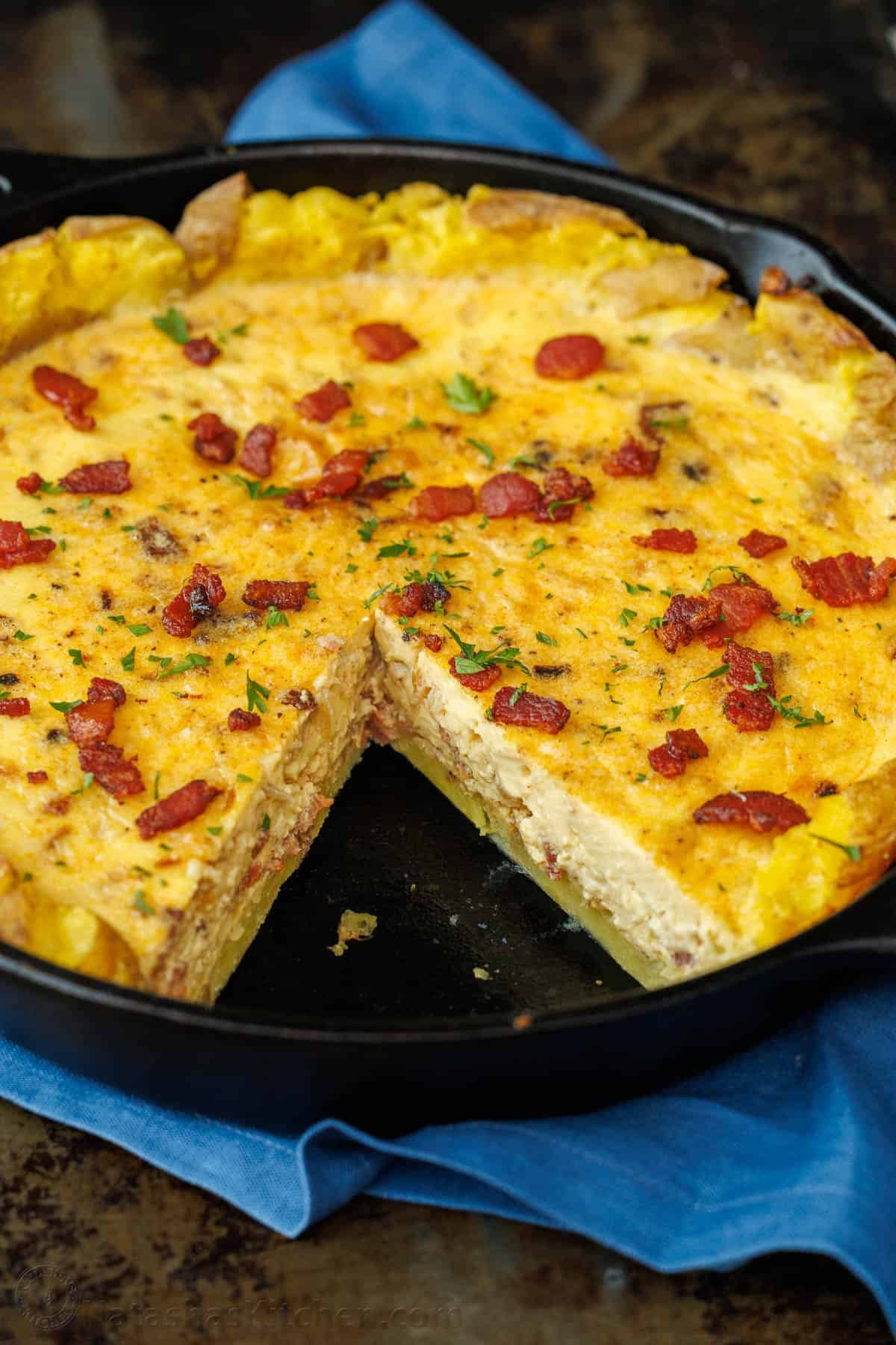 Our Potato Crusted Quiche replaces traditional dough with smashed potatoes for a tasty, gluten-free option that's easy to make and perfect for brunch. Potato Crust Quiche in a 10-inch cast iron skillet with one slice removed, topped with bacon and parsley