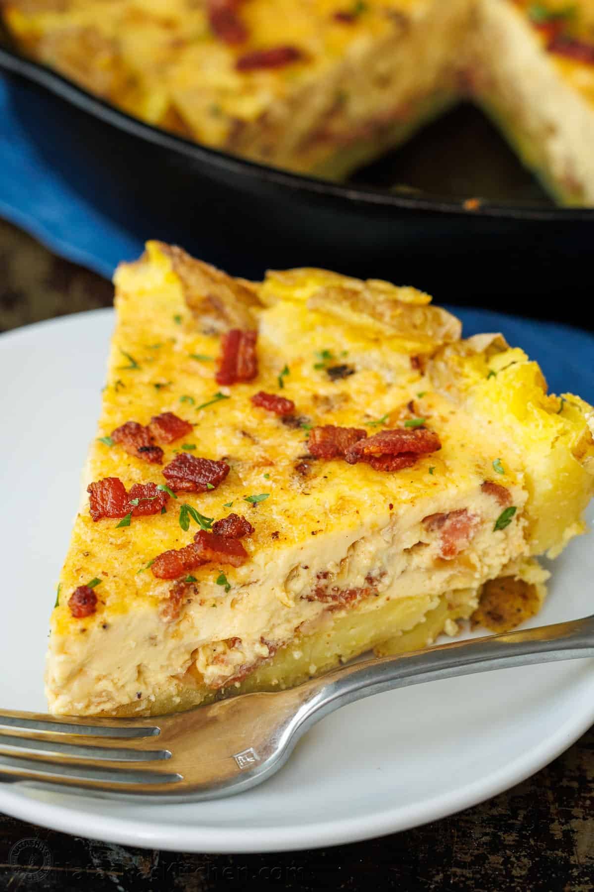 Our Potato Crusted Quiche replaces traditional dough with smashed potatoes for a tasty, gluten-free option that's easy to make and perfect for brunch. A slice of Potato Crusted Quiche topped with bacon and parsley on a plate with a fork.