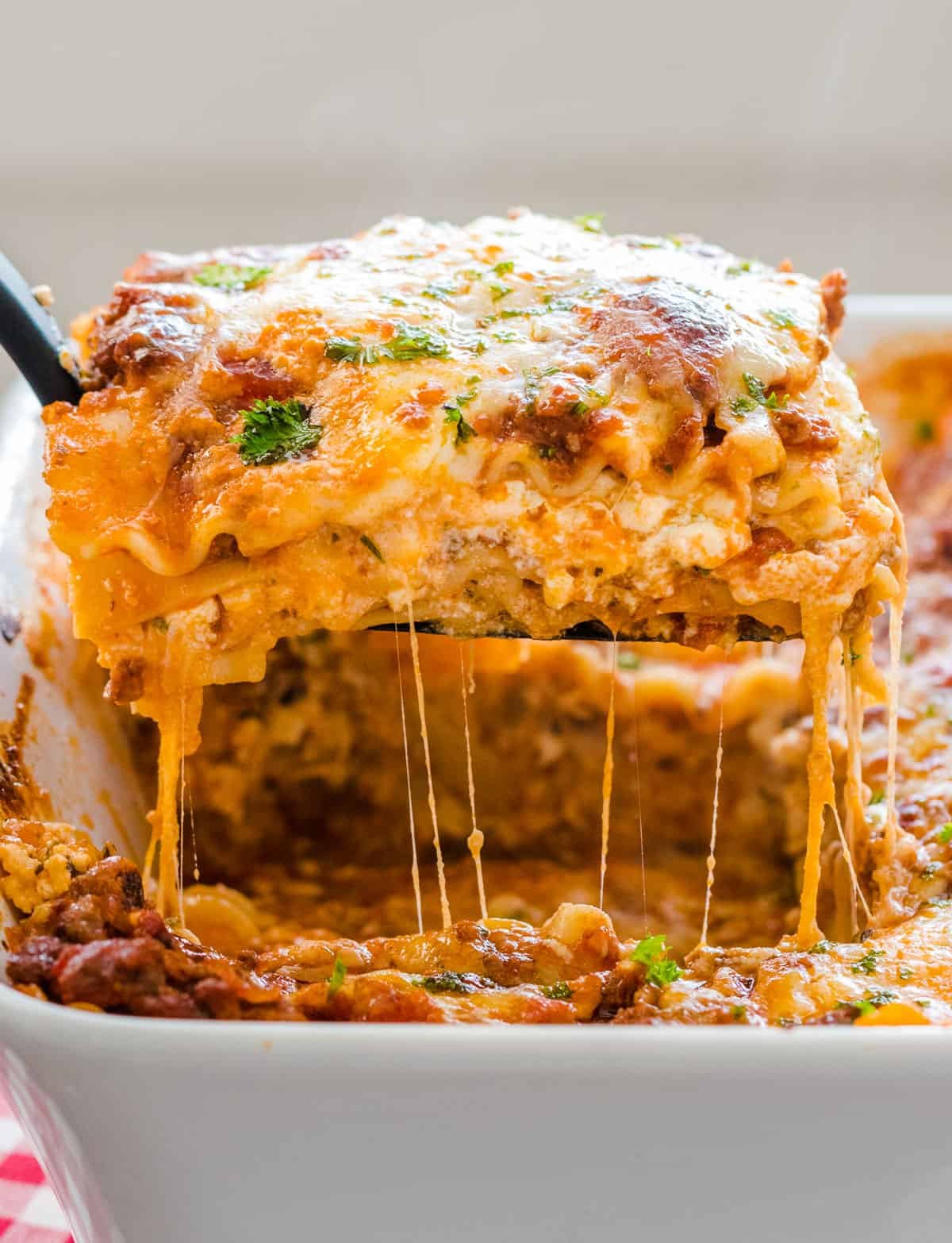 This easy Lasagna Recipe is meaty, cheesy, and flavorful. Perfect for a weeknight dinner or feeding a crowd, readers agree it's the best! Piece of lasagna being lifted from baking dish