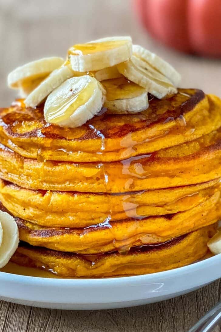 These pumpkin pancakes are so fluffy and the perfect Autumn breakfast. These are easy breakfast pancakes and have wonderful pumpkin flavor. #pumpkinpancakes #pumpkinrecipes Stack of pumpkin pancakes topped with banana and maple syrup
