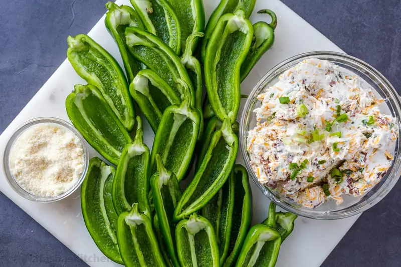 Halved jalapenos on a platter with cream cheese and bacon filling in a bowl.