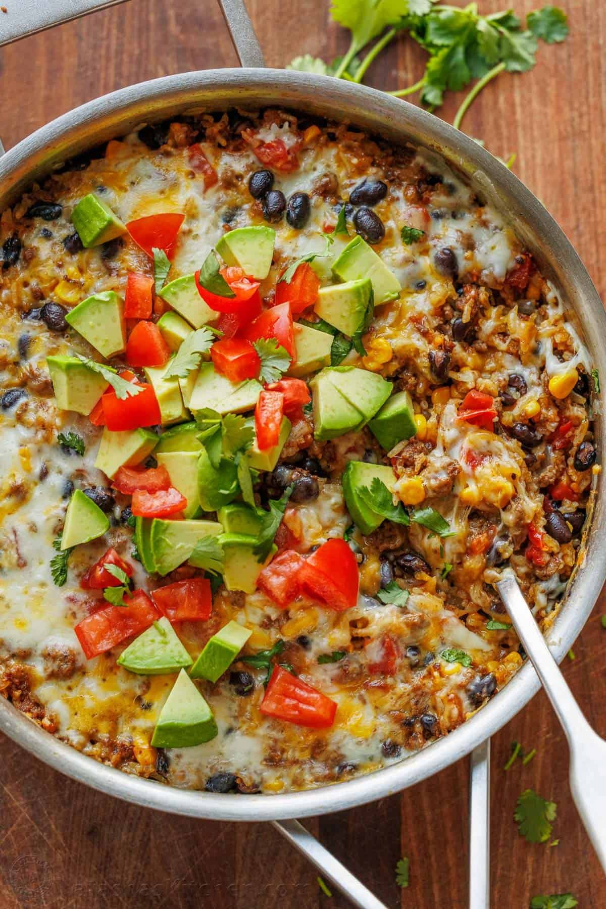 Mexican Ground Beef and Rice Skillet garnished with fresh diced tomatoes, avocado, and cilantro. Ready to serve with a spoon.